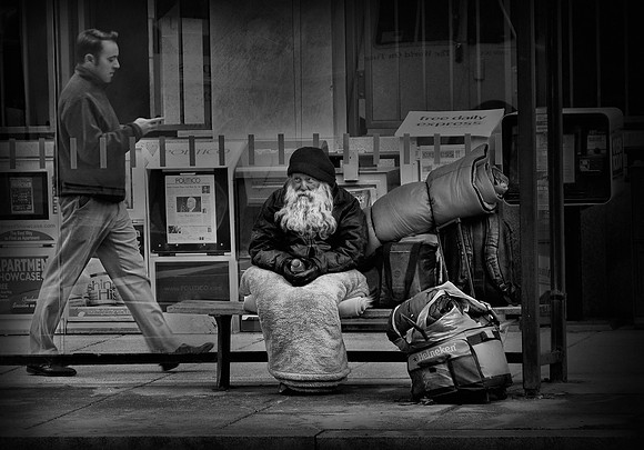 "2bsy2care" A man checking his phone walks past a homeless man on the street.        By: Dan Francis